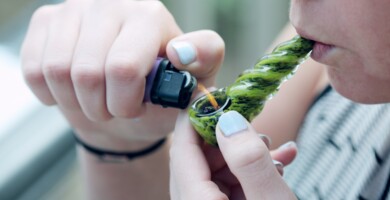 Frau zieht an einer Cannabispfeife die sie mit einem Feuerzeug anzündet