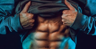 mann_mit_sixpack_muskeln_und_hoodie_blau_beleuchtet_vor_schwarzem_hintergrund