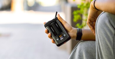 Person am Straßenrand sitzend, die einen Vaporizer in der Hand hält an einem sonnigen Tag