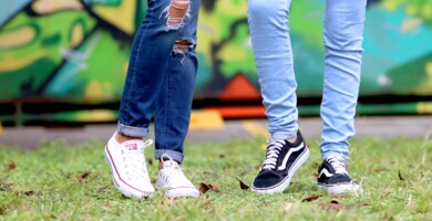Zwei Beinpaare junger Personen vor einer Grafittiwand im Hintergrund
