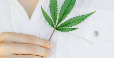 Frau mit weißem Hemd die sich ein Cannabisblatt vor die Brust hält