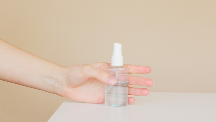 Hand die eine Sprüflasche mit klarer Flüssigkeit auf einem Tisch hält