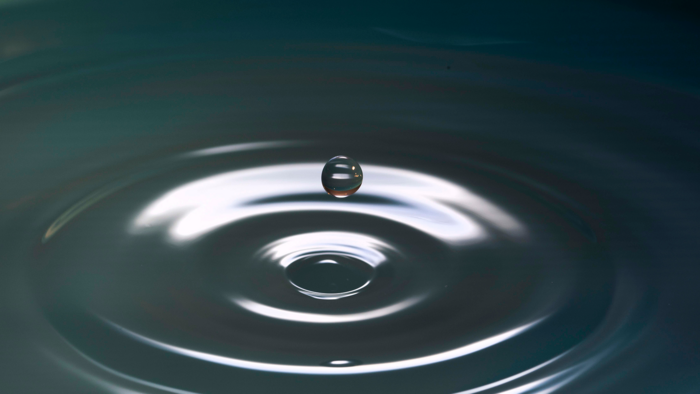Wassertropfen welcher aus dem Wasser entspringt und typische Wasserkreise zeichnet