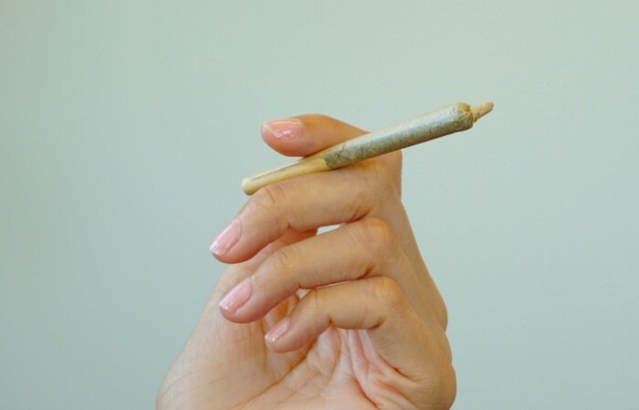 frauenhand_mit_joint_zwischen_den_fingern_vor_weissem_hintergrund