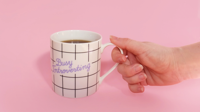 Hand die einen Kaffeebecher vor einem pinken Hintergrund hält