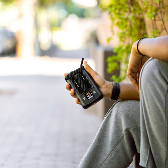 Person am Straßenrand sitzend, die einen Vaporizer in der Hand hält an einem sonnigen Tag