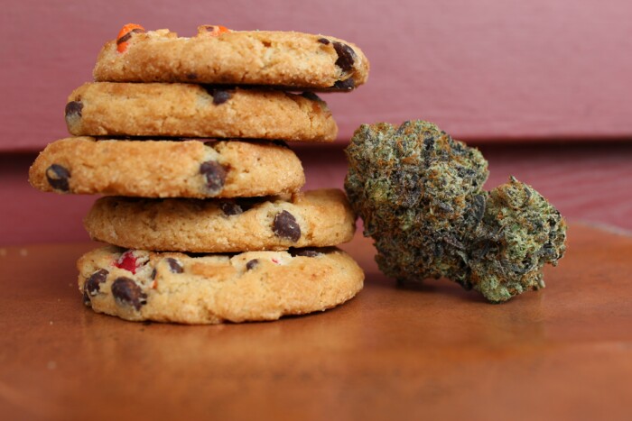 Space Cookies mit Cannabis Blüte auf einem Holztisch mit rotem Hintergrund