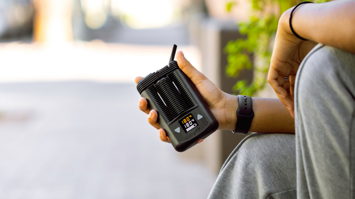 Person die einen Vaporizer in der Hand hält am Rande eines Fußgängerwegs