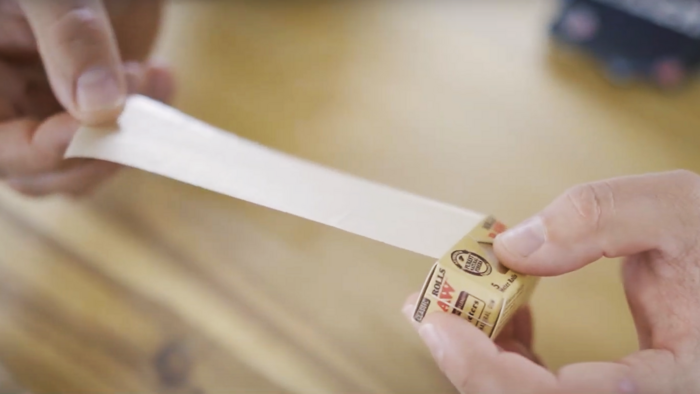 Zwei Hände die eine Rolle Endlospapier für Joints abwickeln vor einem Holzbrett