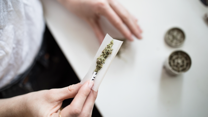 Hände die einen Joint rollen vor einem weißen Tisch auf dem ein Grinder steht