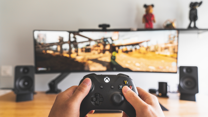 Hände die einen Controller für eine Spielkonsole halten vor einem Widescreen-Bildschirm