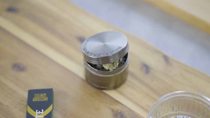 Metallener Grinder mit etwas Cannabis auf einem Holzbrett