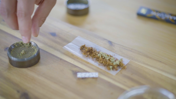 Hand die etwas Cannabis in einen vorbereiteten Joint legt auf einem Holzbrett