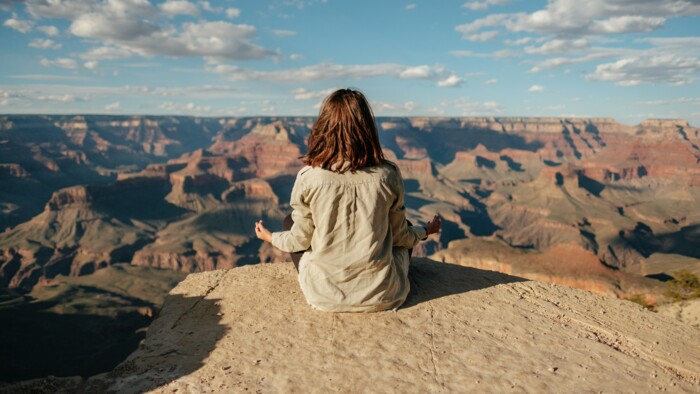 Meditierende Frau vor dem Grand Canyon bei schönem Wetter und blauem Himmel
