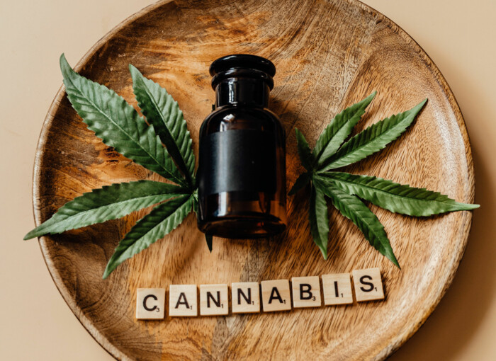 Medizinisches Fläschchen auf einem Holzteller mit Cannabisblättern geschmückt