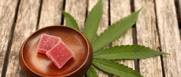 suessigkeit_in_einer_schale_daneben_cannabis_blatt_auf_holzbohlen