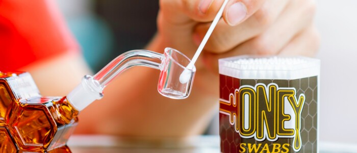 Hand die ein Wattestäbchen mit Cannabiskonzetrat in ein Dabbing Rig gibt