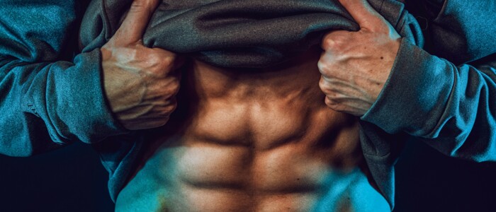 mann_mit_sixpack_muskeln_und_hoodie_blau_beleuchtet_vor_schwarzem_hintergrund