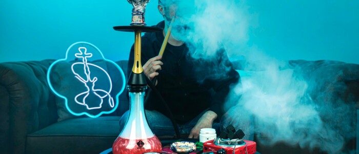Person die auf einem Sofa sitzt und eine Wasserpfeife raucht die mit rotem Wasser gefüllt ist