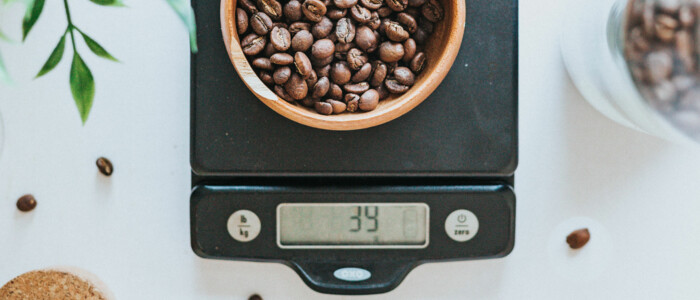 Feinwaage mit Kaffeebohnen auf einem weißen Tisch mit einer Pflanze