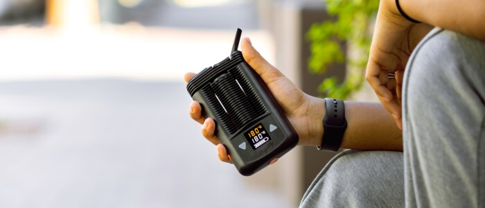 Person am Straßenrand sitzend, die einen Vaporizer in der Hand hält an einem sonnigen Tag