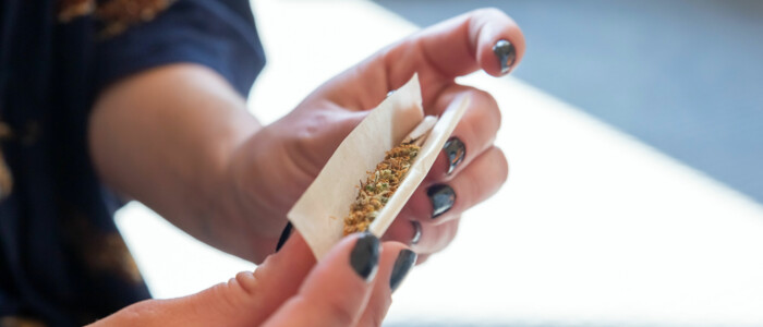 Frau die einen Joint rollt mit Sonnenschein im Hintergrund