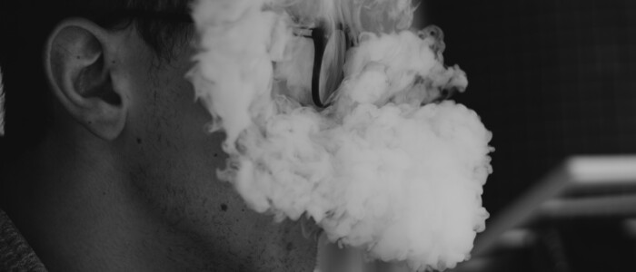 Brille tragender Mann der in eine Rauchwolke gehüllt ist in schwarz-weiß