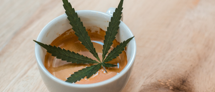 Eine Tasse Kaffee in welcher ein Hanfblatt liegt auf einem hölzernen Tisch