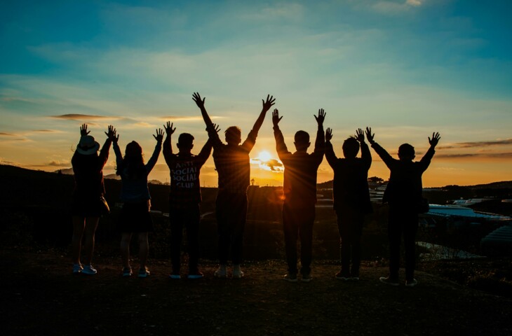 menschen_im_gegenlicht_bei_sonnenuntergang_mit_erhobenen_haenden